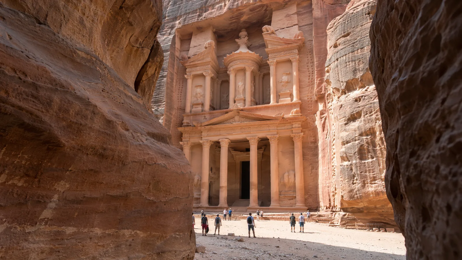 The Treasury at Petra viewed from the sandstone passage, with visitors for scale.